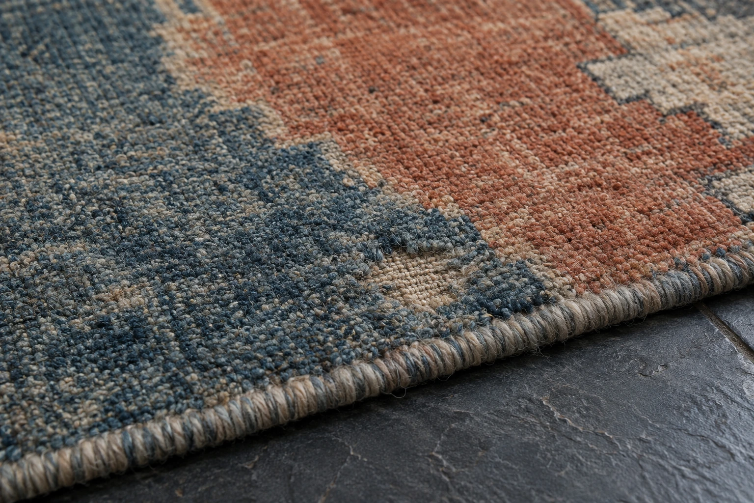 Close view of a blue and rust wool rug with a small area of missing pile near its bound edge