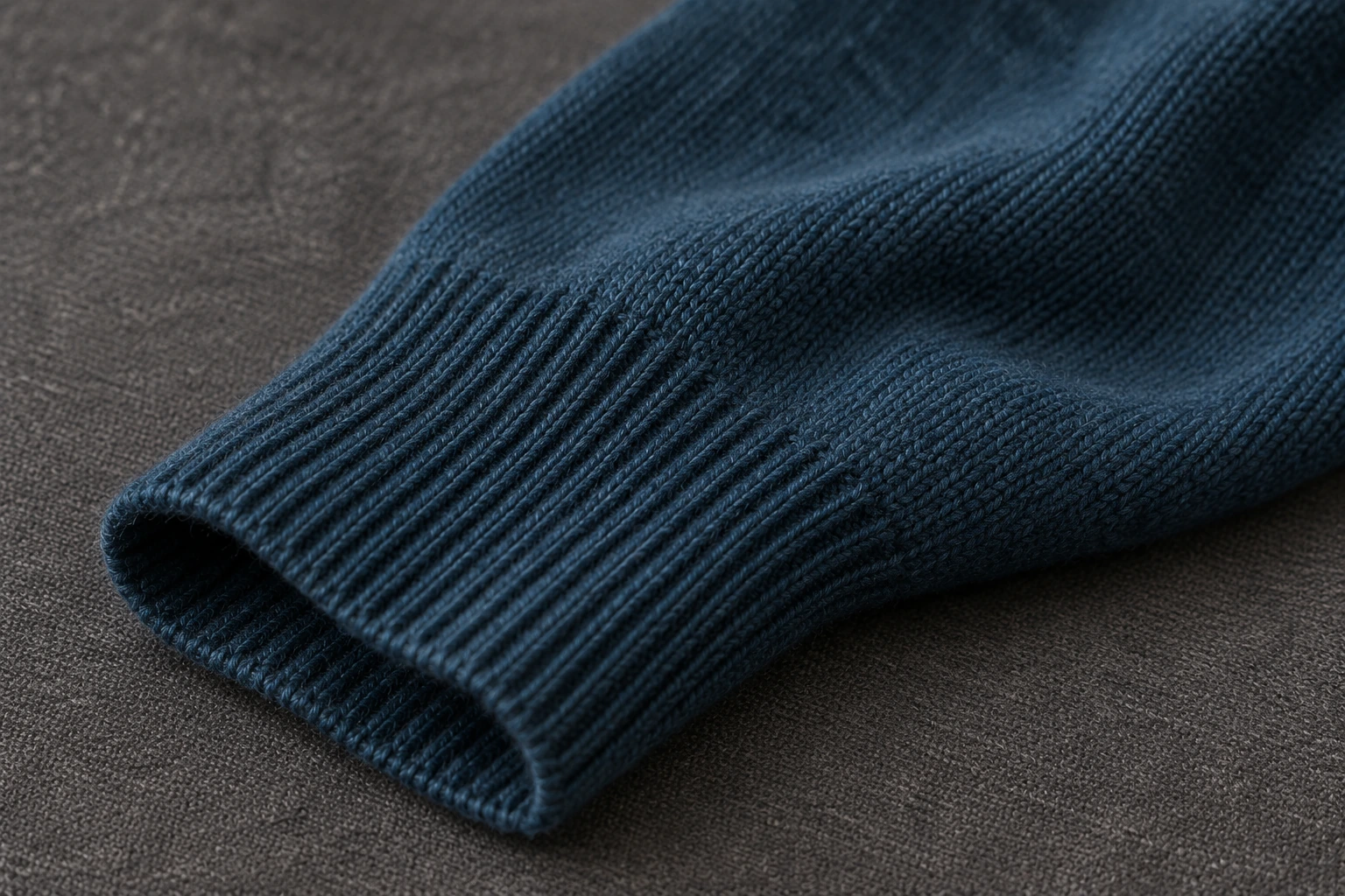 Close-up of deep petrol-blue Merino wool knit sleeve and ribbed cuff with realistic fine stitches