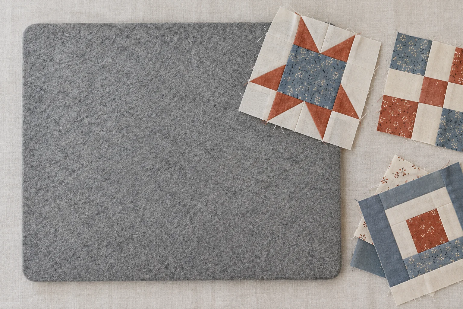 Wool pressing mat beside unfinished cotton patchwork pieces on a sewing surface.