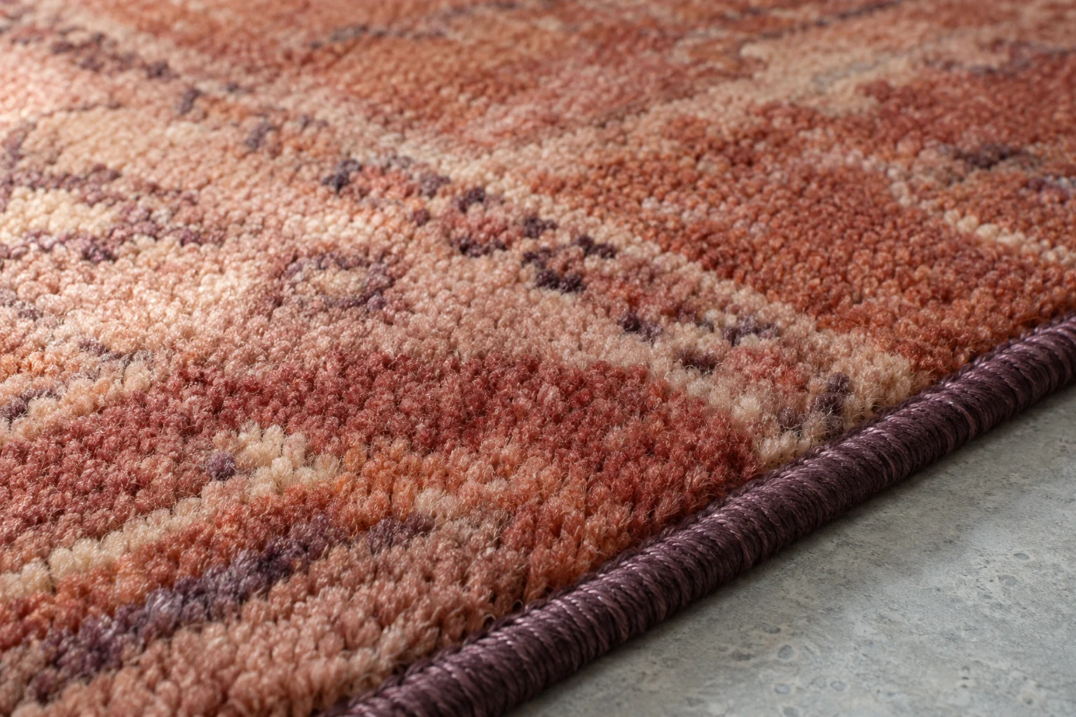 Close-up of terracotta wool rug pile and a dark bound edge on a pale gray floor